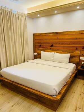 A neatly made bed with a wooden headboard, a bedside table with a phone, and a curtain to the left. - Mak Hotel (Bengaluru)