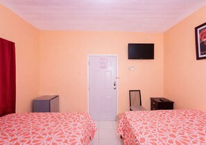 A hotel room with two beds, a TV, a door, and a small desk.
