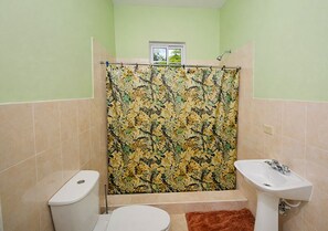 A bathroom with a toilet, sink, shower curtain, and a window.