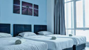 A hotel room with three beds, a large window with curtains, and two landscape paintings on the wall.