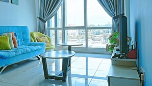 A living room with a blue sofa, a yellow armchair, a small round table, and a TV on a stand. - reStary Blue Game Themed Homestay (Kota Kinabalu)