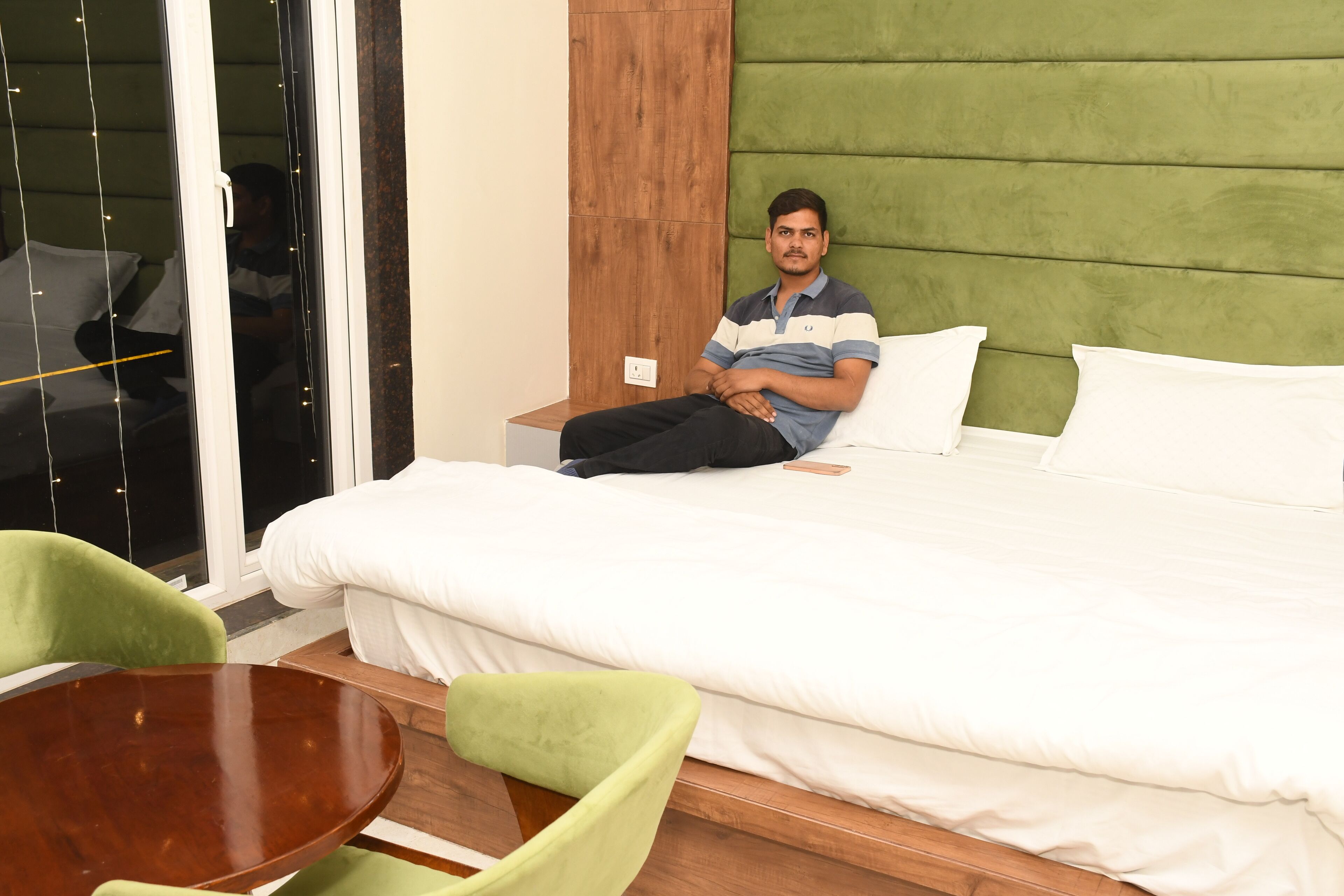 A hotel room with a bed, a wooden nightstand, a green upholstered headboard, and a green chair.