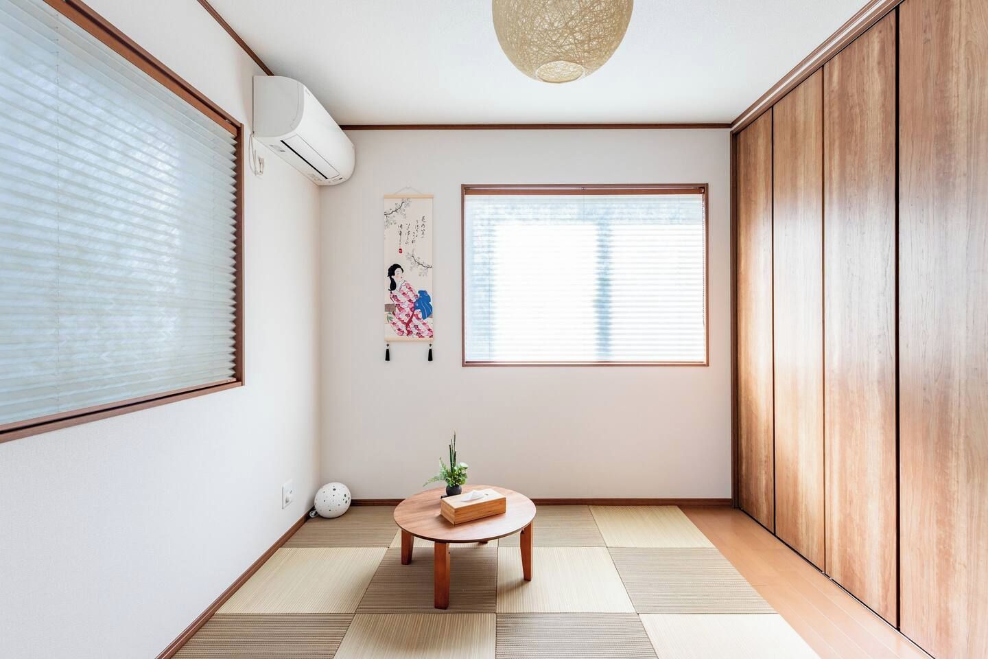 A room with tatami flooring, a shoji screen, a traditional Japanese artwork, and a ceiling fan.