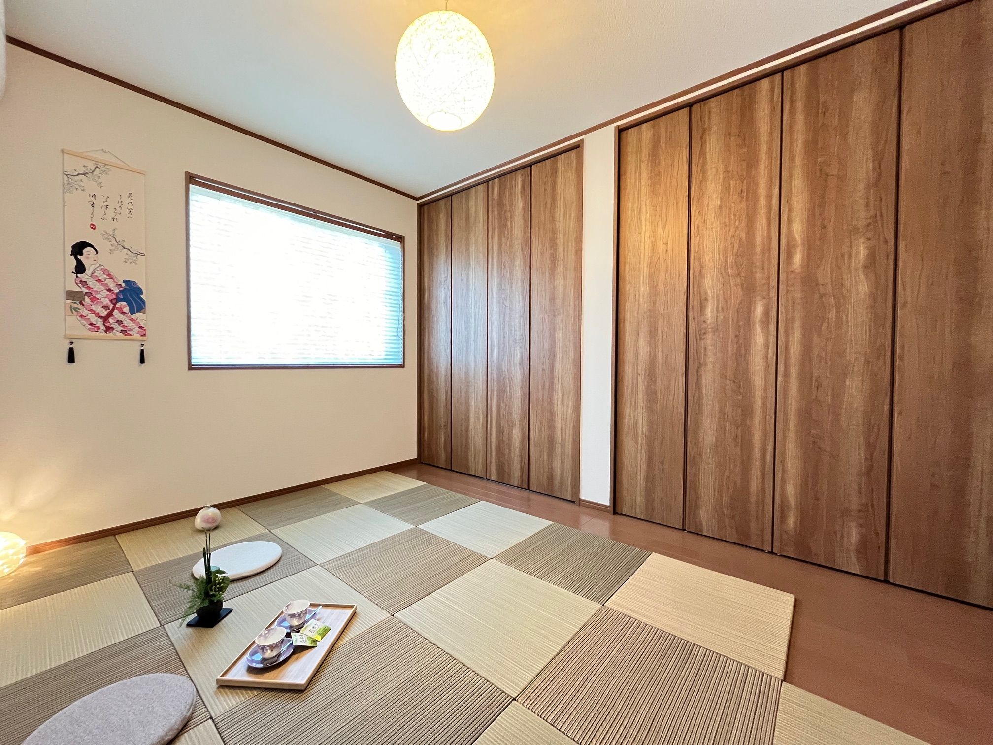 Una habitación con suelo de tatami, una puerta corredera de madera, un ventanal grande y una obra de arte japonesa tradicional.
