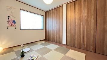 Una habitación con suelo de tatami, una puerta corredera de madera, un ventanal grande y una obra de arte japonesa tradicional.