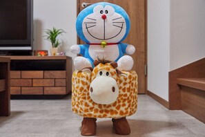 Une peluche représentant un personnage bleu et blanc déguisé en girafe, posée sur un sol recouvert d’une moquette.