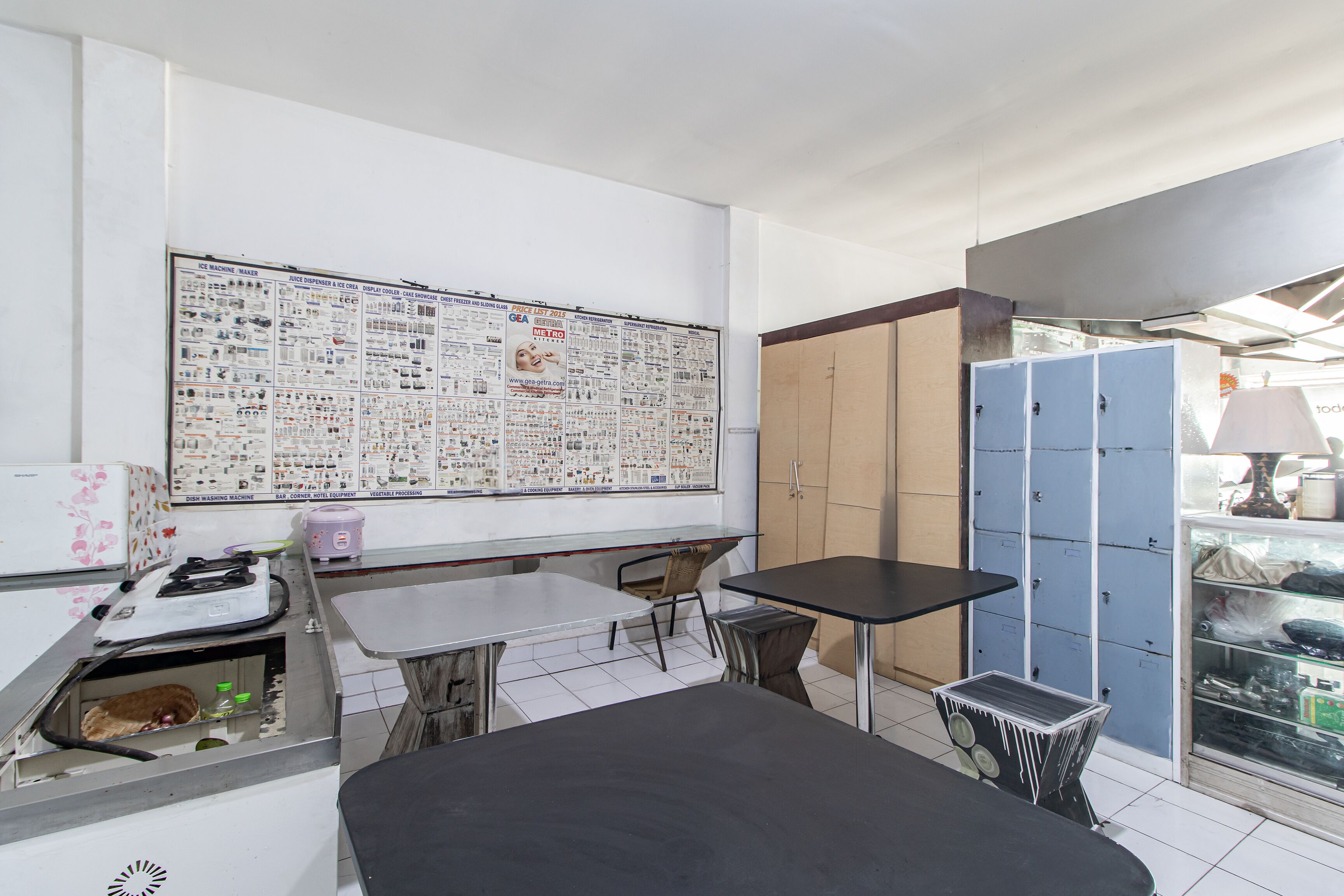 Una habitación con un cartel informativo grande, una mesa, sillas, un armario y un mostrador con un lavabo.