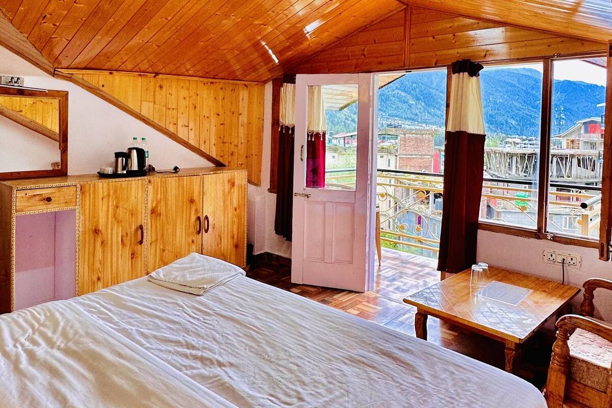 A wooden cabin with a large bed, a small table, and a view of a town through a window.