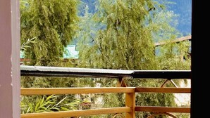 A balcony with a metal railing featuring floral designs, overlooking a mountainous landscape with dense green trees and a cloudy sky. - Royal Selection (Manali)