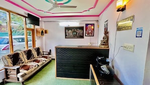 A reception area with a sofa, a desk, a statue, and a ceiling fan. - Royal Selection (Manali)