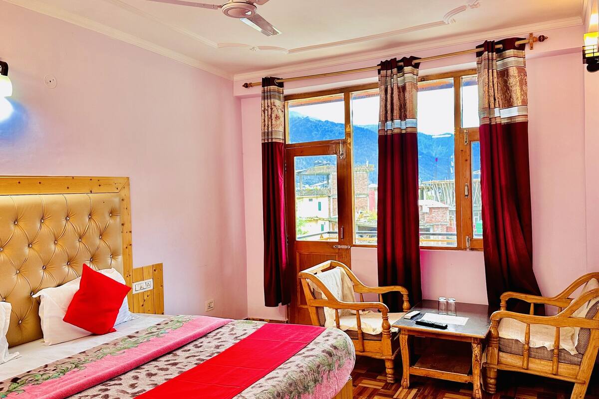 A hotel room with a bed, a table, chairs, a window with curtains, and a ceiling fan.