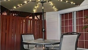 En udendørs terrasse med et bord og stole under en stor parasol med lyskæder.