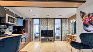 Una cocina moderna con microondas, estufa y lavabo. Hay un televisor en el centro de la habitación y una silla azul en primer plano.