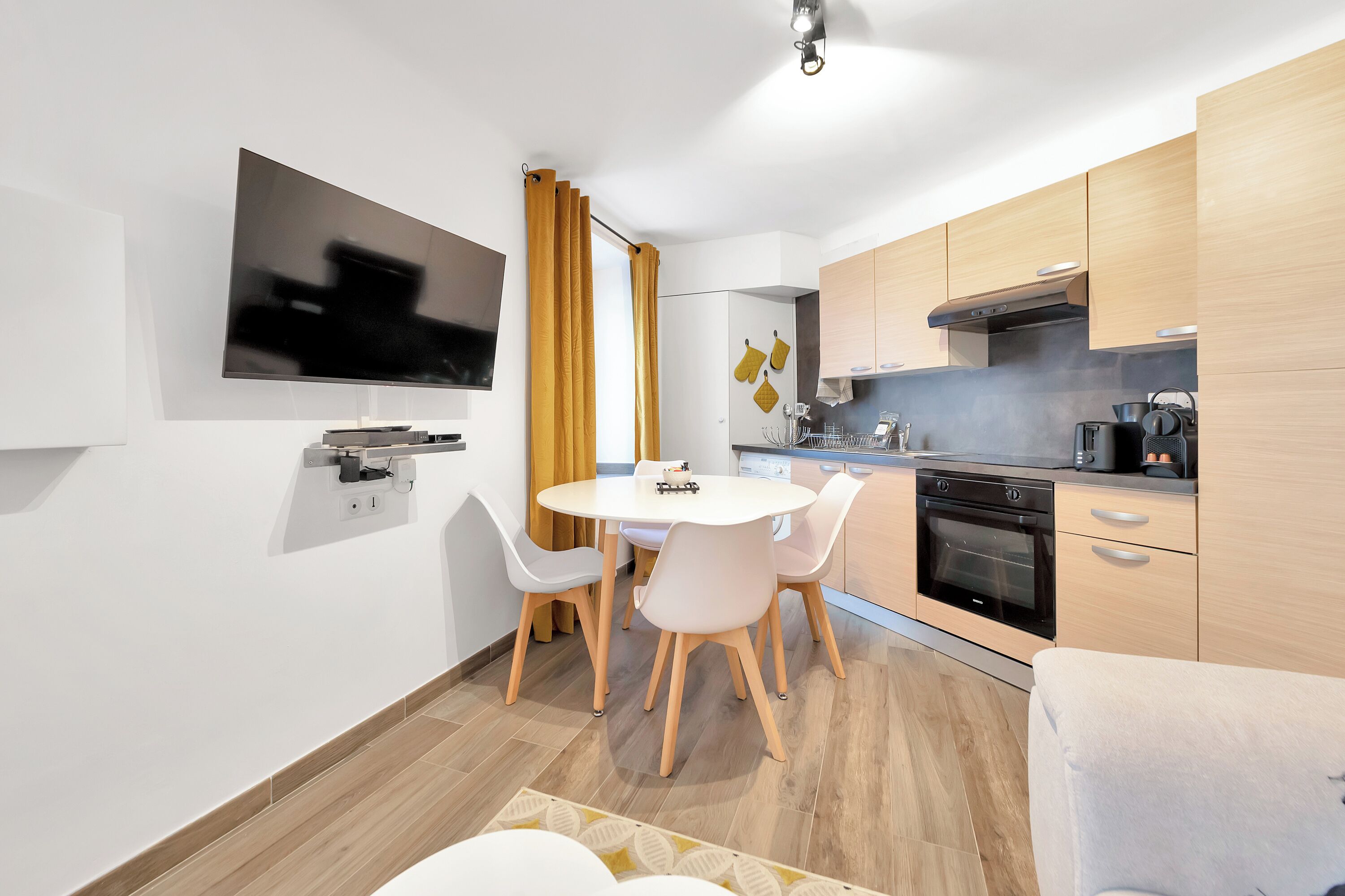 A modern kitchen with wooden cabinets, a built-in oven, and a dining area with a round table and chairs.