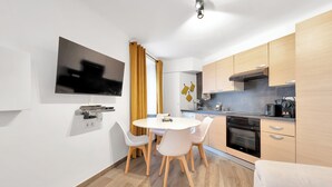 A modern kitchen with wooden cabinets, a built-in oven, and a dining area with a round table and chairs. - Le Palme D'or près de la Croisette et Palais (Cannes)