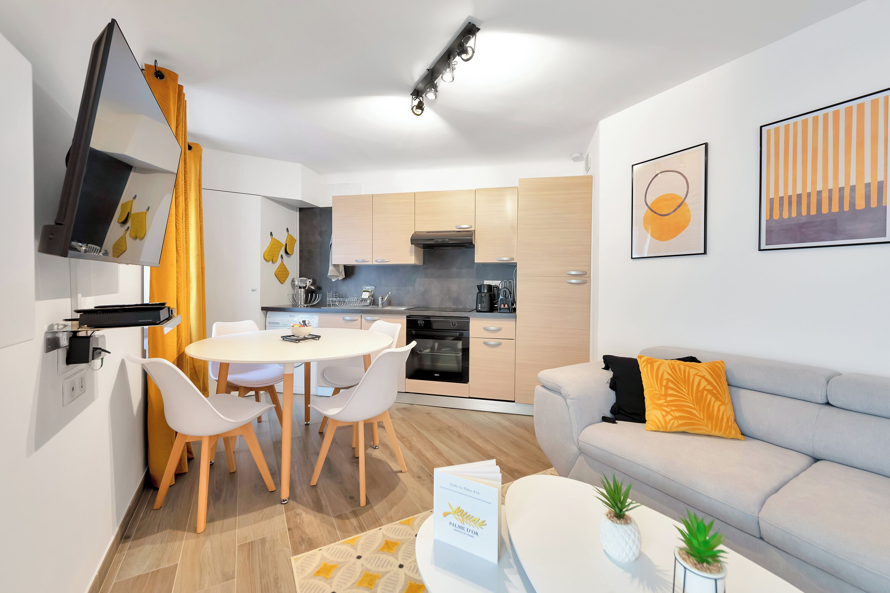 A modern kitchen with a dining area, a sofa, and a coffee table with plants.