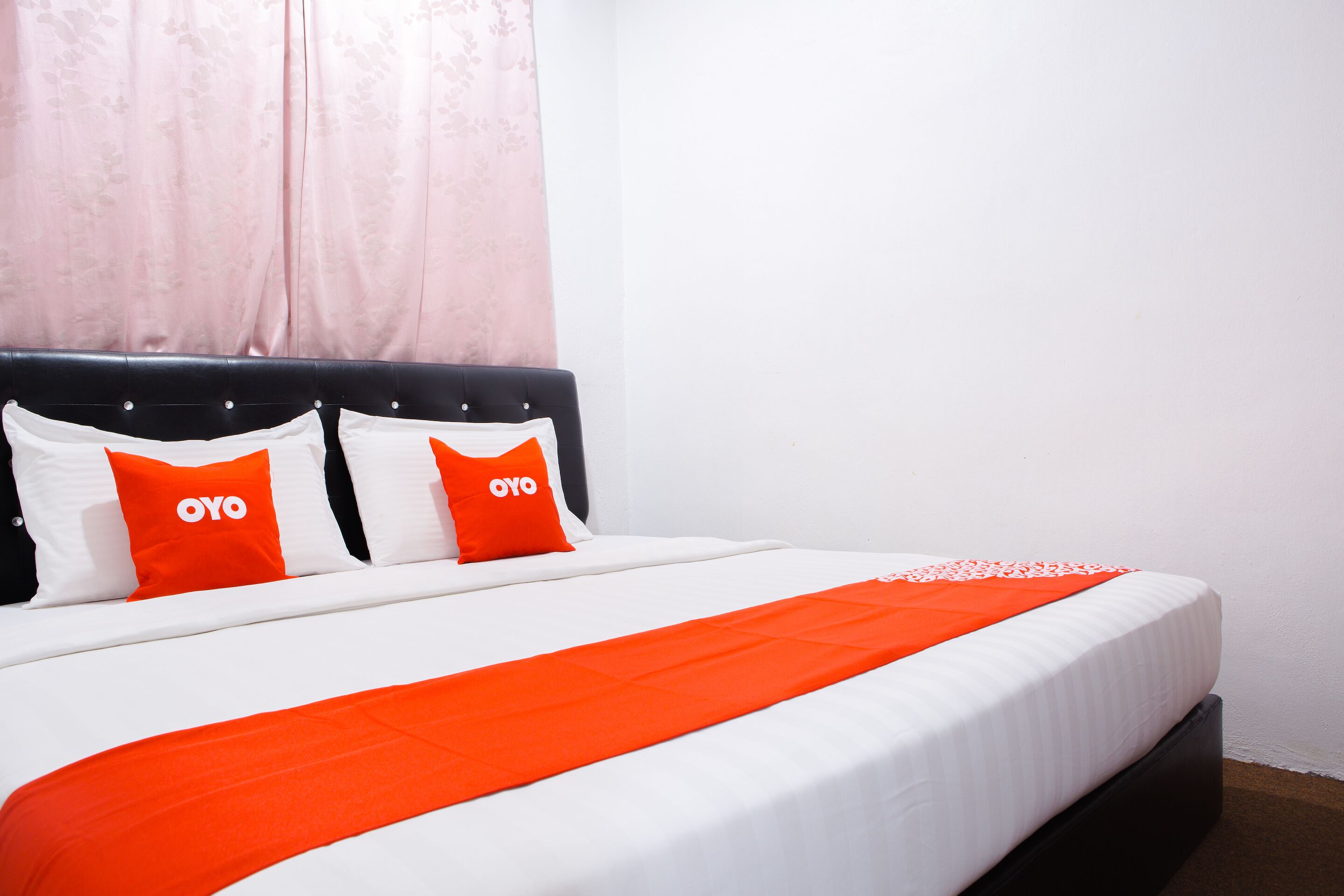 A bed with white and orange bedding, two pillows with the "OYO" logo, and a red blanket.