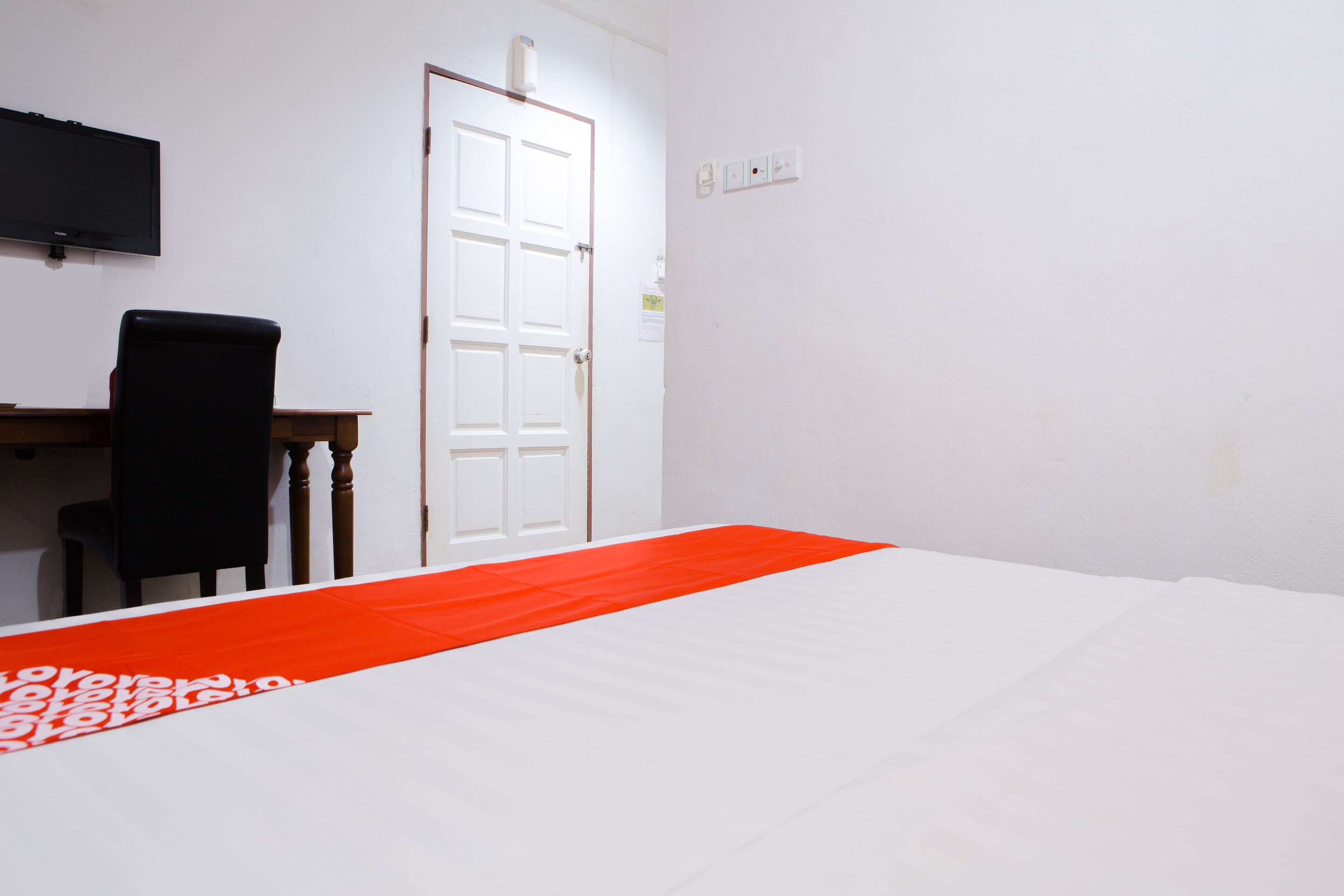 A room with a bed, a desk, a chair, a television, and a door.