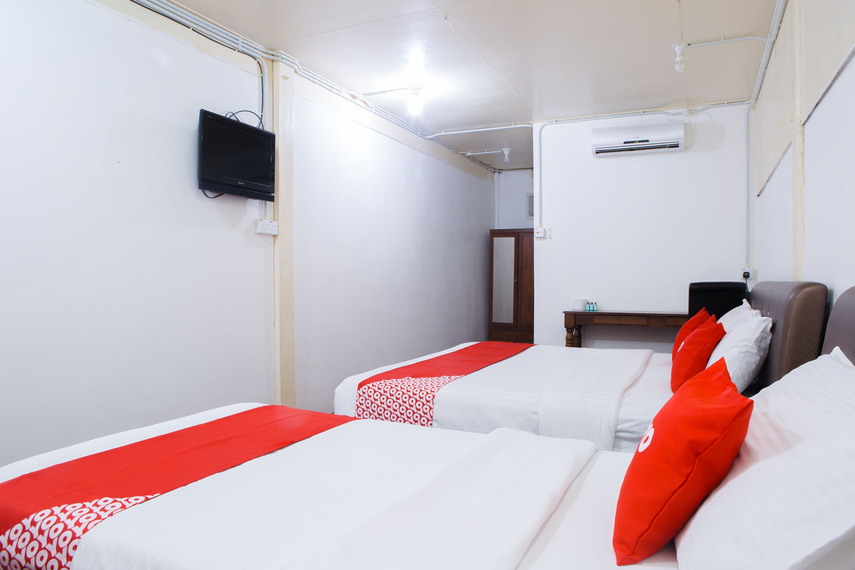 A hotel room with two beds, a TV, an air conditioner, and a small table.