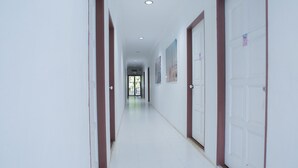 A long, narrow hallway with white walls and brown trim, leading to a door at the end. - Hotel O The 7 Lodge Tambunan (Tambunan)