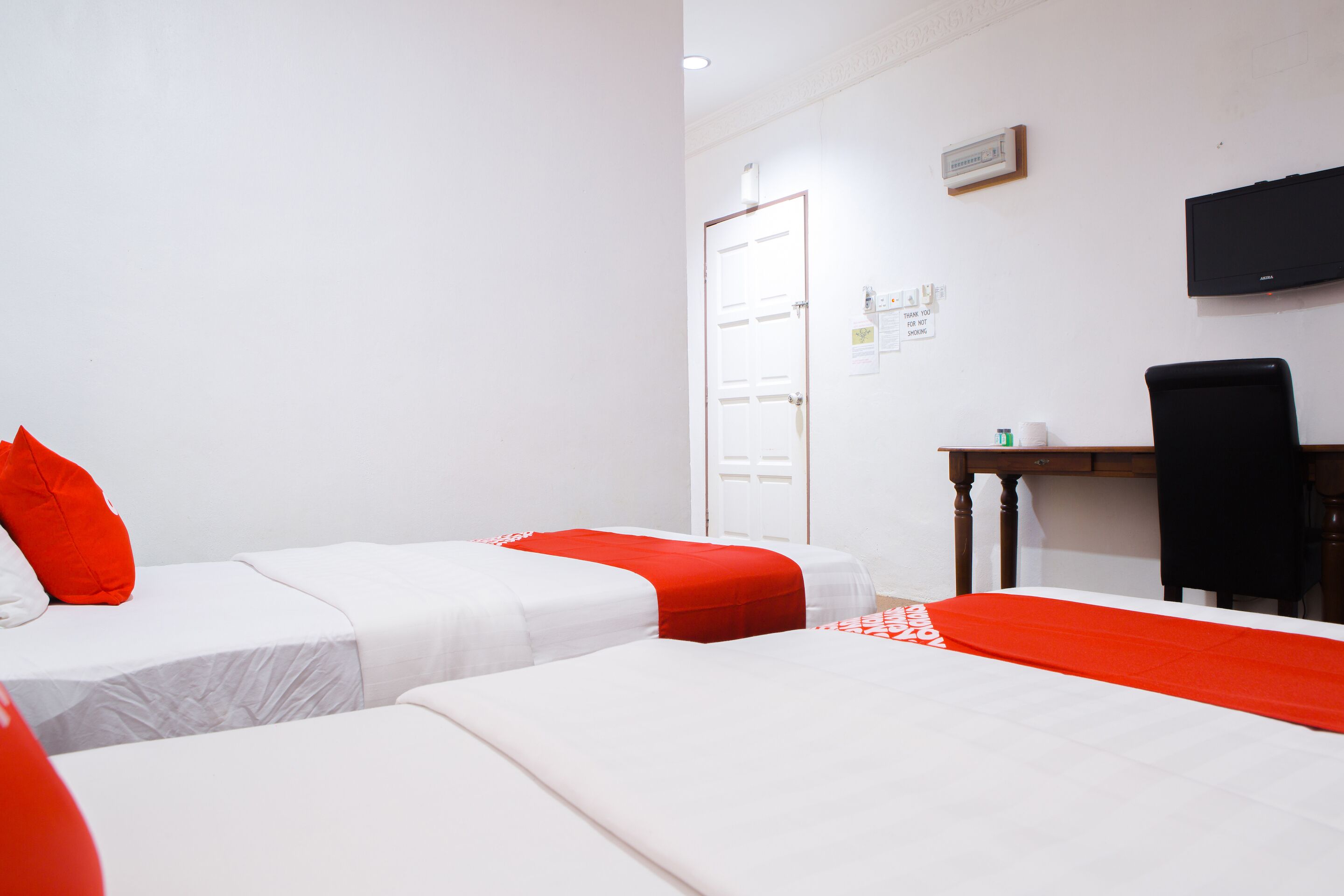 A hotel room with two beds, a desk, a chair, a television, and a door.
