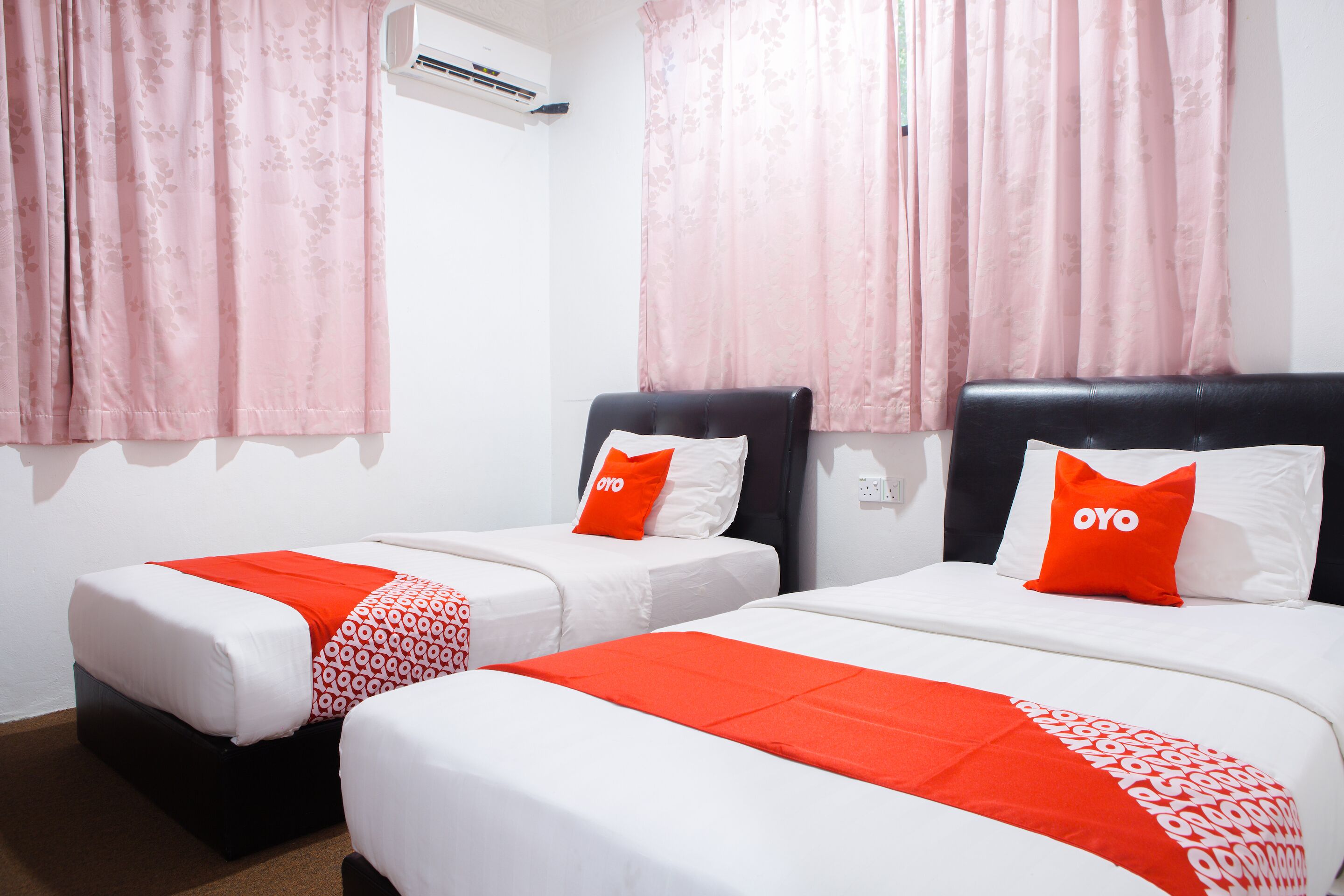 Two single beds with white and red bedding, pink curtains, and a black headboard.