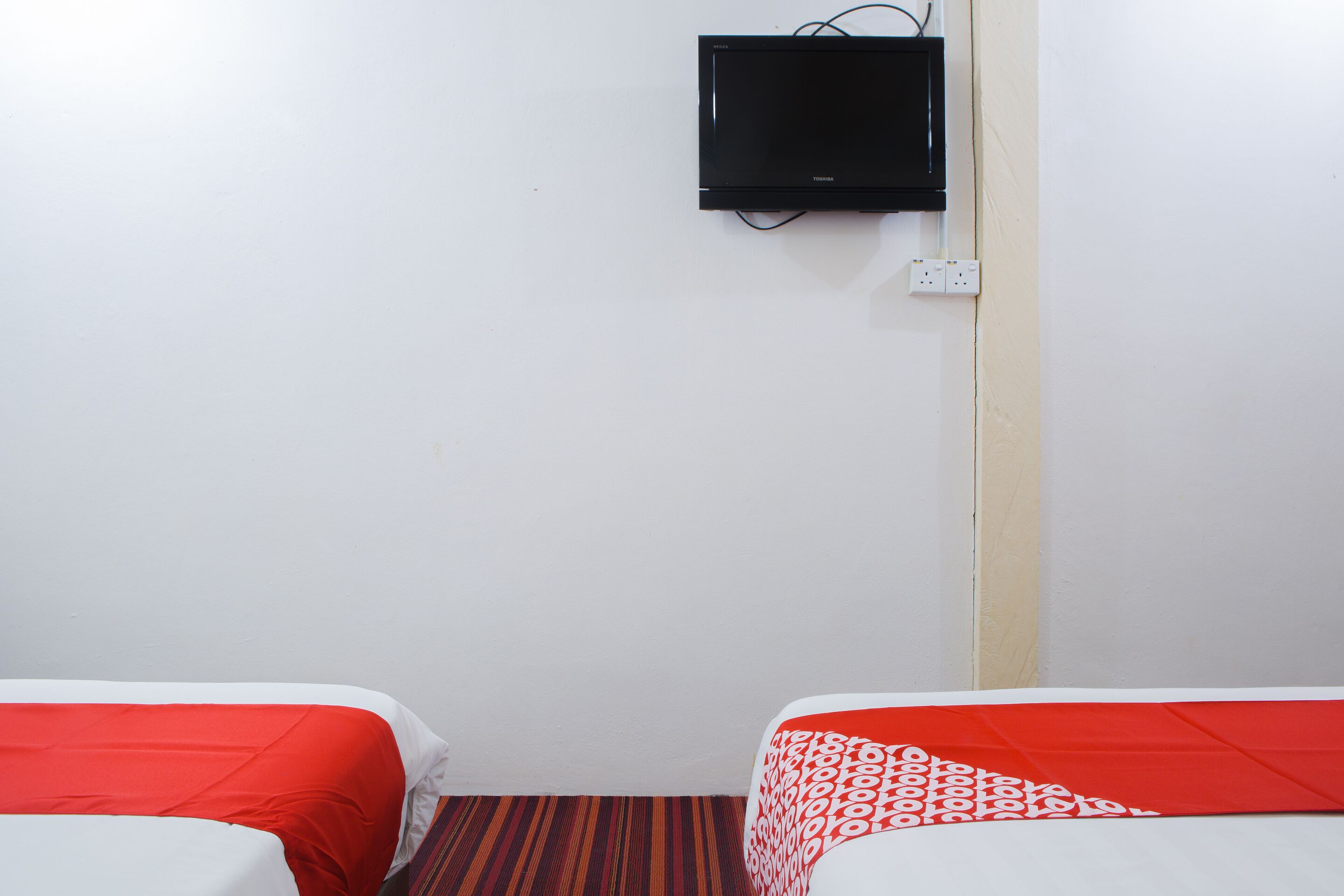 Una habitación de hotel con dos camas, un televisor montado en la pared y un enchufe.
