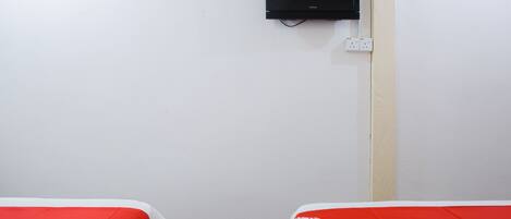 Una habitación de hotel con dos camas, un televisor montado en la pared y un enchufe.