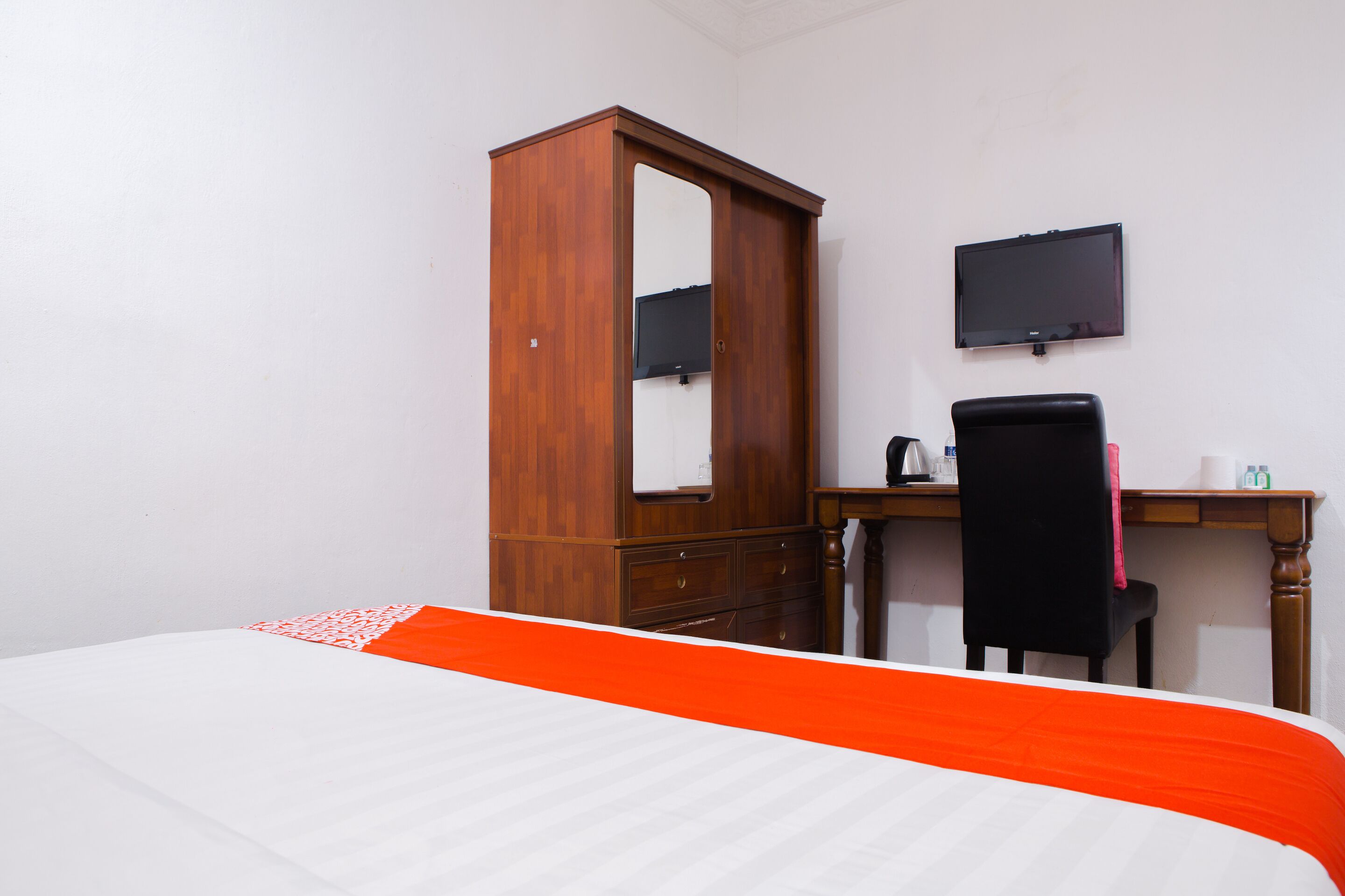 Un dormitorio con una cama, un armario de madera, un escritorio con silla y un televisor de pantalla plana en la pared.