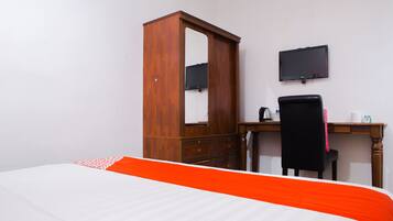 Un dormitorio con una cama, un armario de madera, un escritorio con silla y un televisor de pantalla plana en la pared.