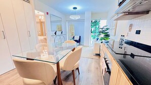 A modern kitchen with a glass dining table, white chairs, and a black stove. - Surco Polo Suites (Lima)