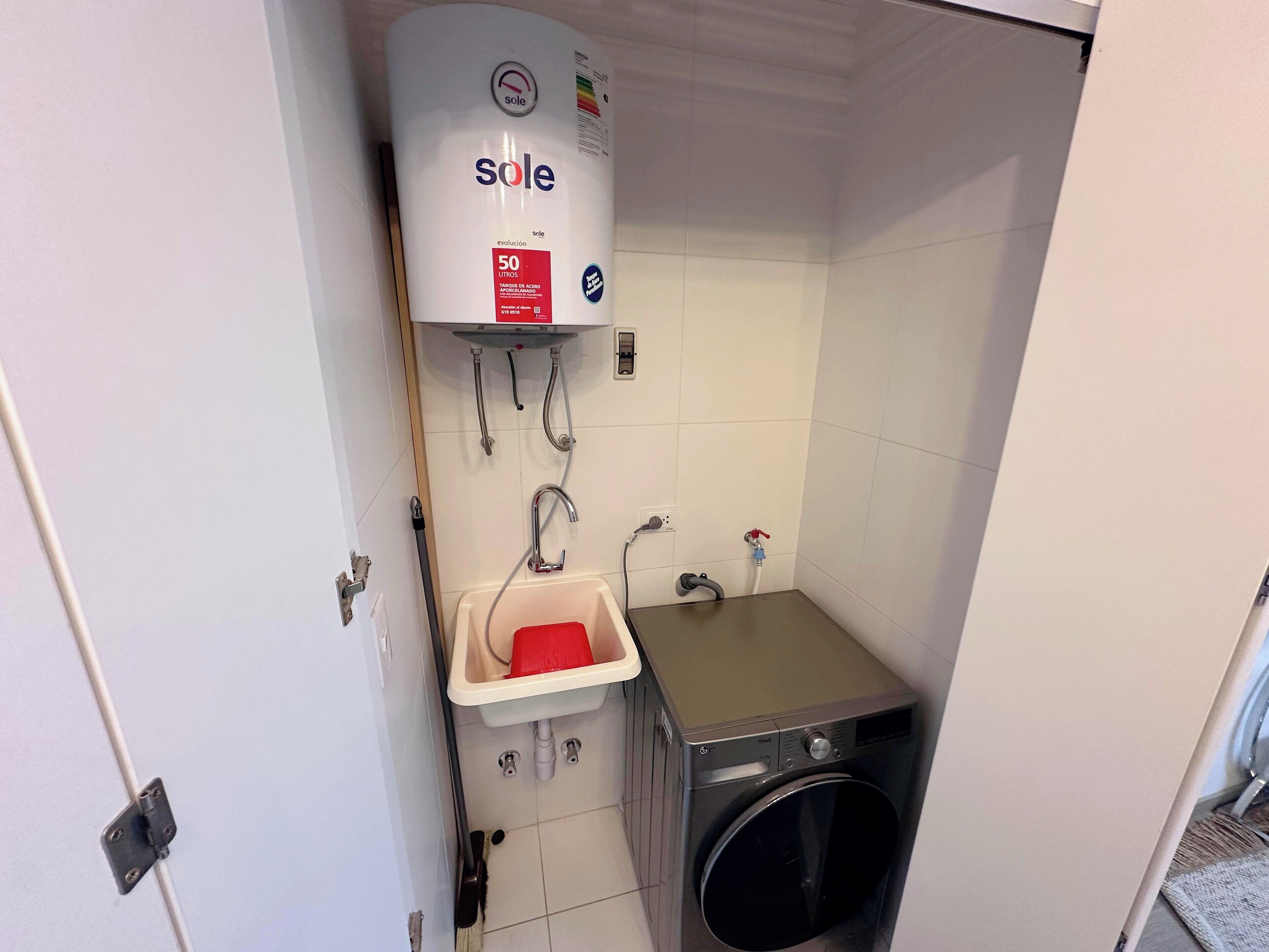 Une petite buanderie équipée d’un lave-linge, d’un évier et d’un chauffe-eau.