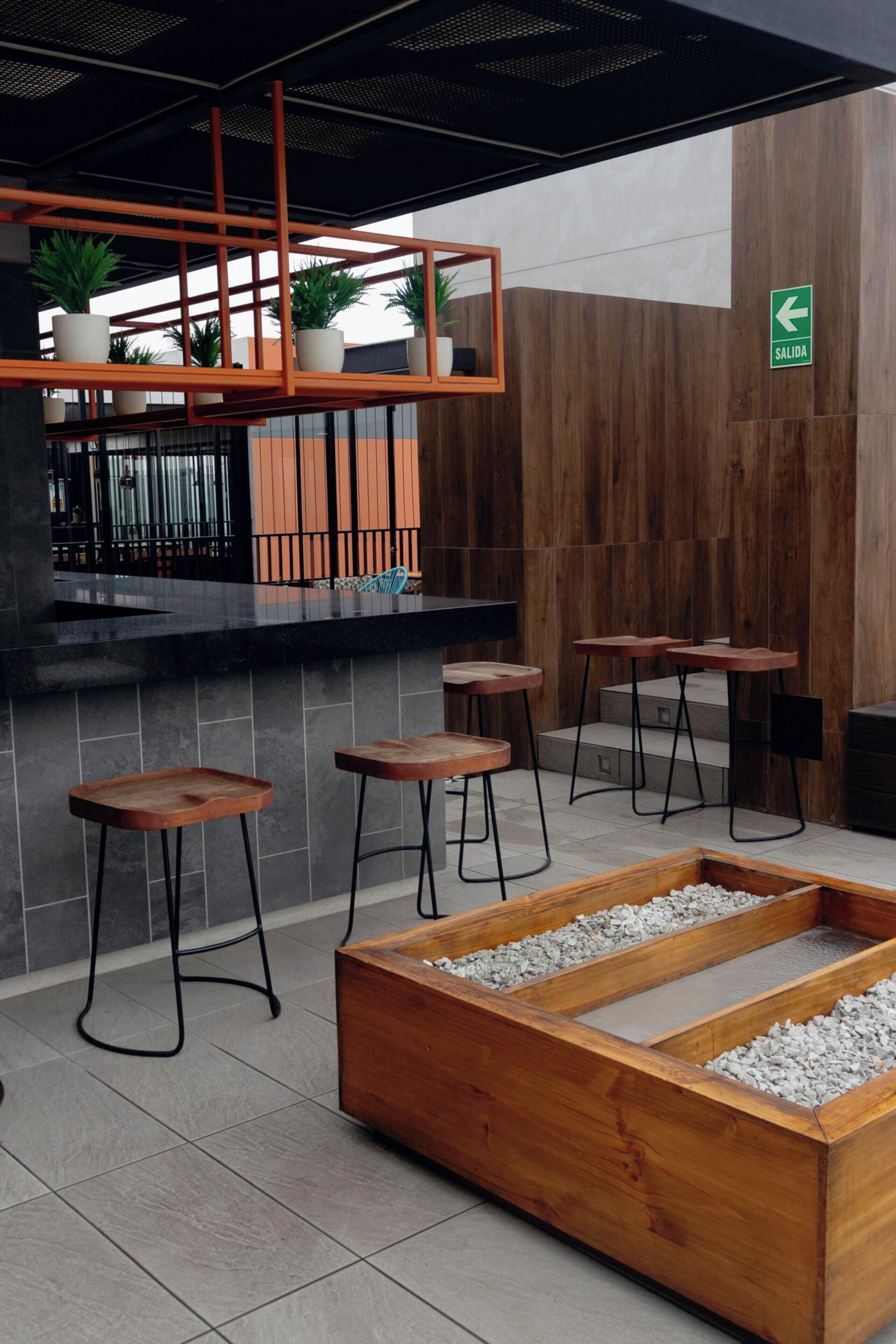 Een moderne bar met een houten toonbank, barstoelen en een zithoek met een houten plantenbak.
