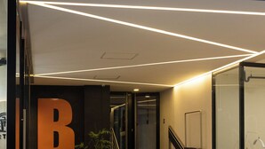 Entrada de un edificio moderno con un gran letrero 'B', una escalera y una planta en maceta.