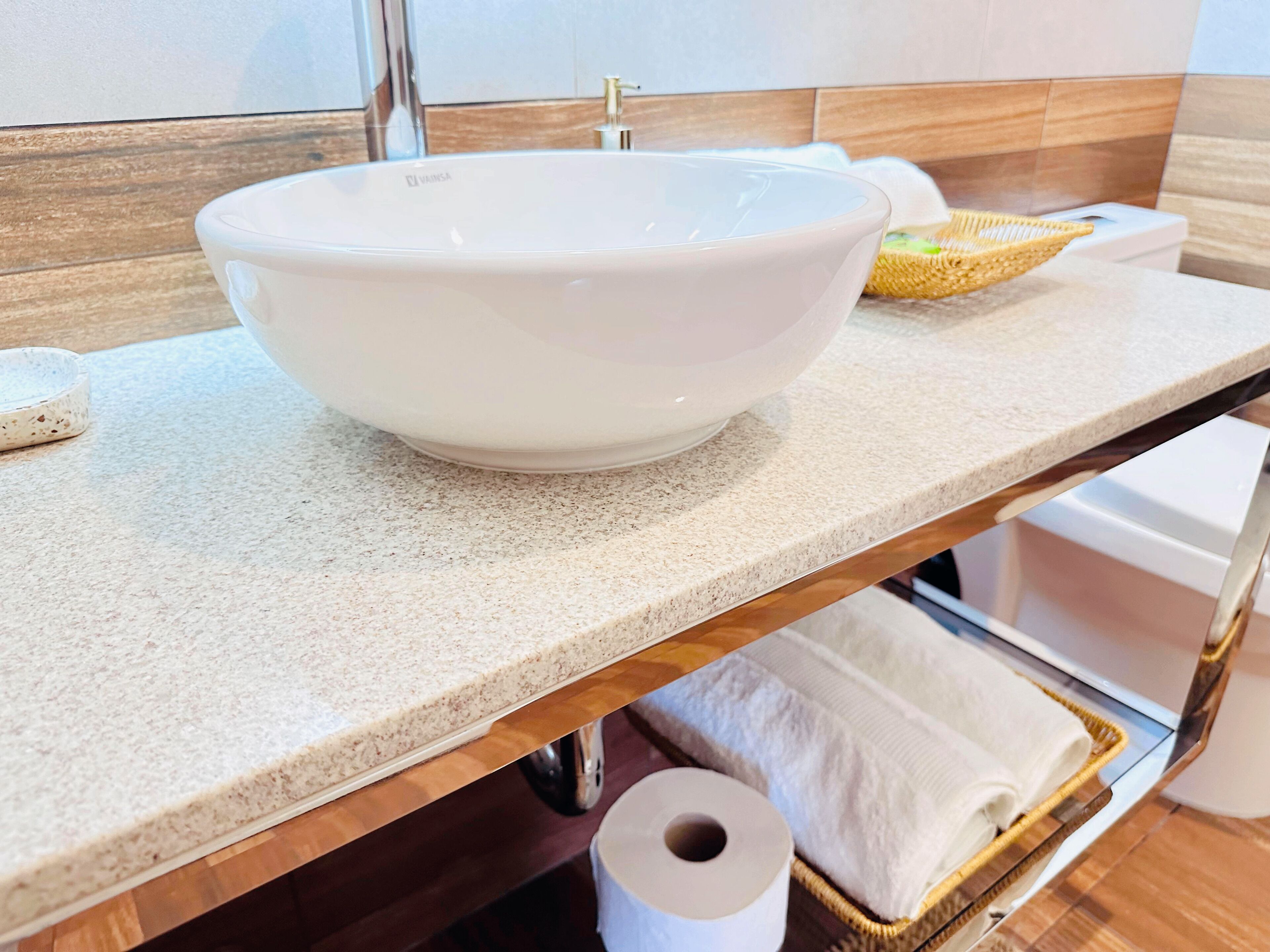 A bathroom with a white sink, a wooden countertop, a basket with towels, and a toilet paper roll.