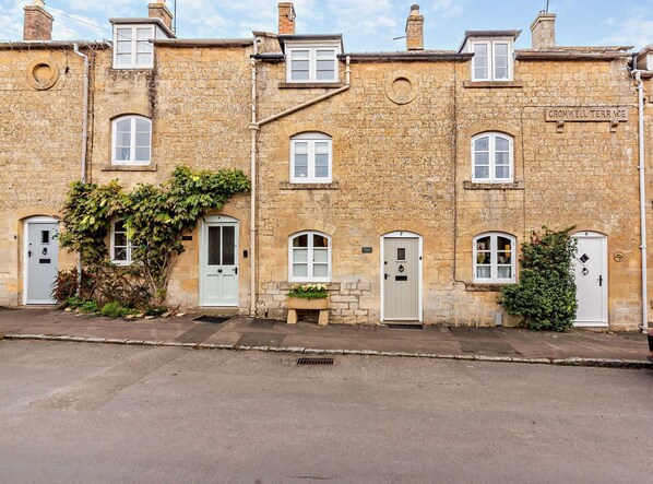 A row of stone buildings with numbered doors, a bench, and a sign reading 'CROMWELL TERRACE'. - Cosy yet stylish Cotswold holiday cottage - Rosewood Cottage (Blockley)