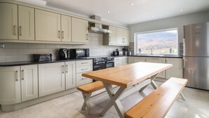 A modern kitchen with light-colored cabinets, a wooden table, and a built-in oven. - Craig Yr Ronwy (Bala)