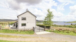 A two-story house with a fenced yard, a wooden deck, and a view of a lake and hills in the background. - Craig Yr Ronwy (Bala)