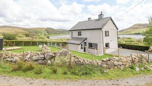 A two-story house with a stone wall in front, a grassy yard, and a lake in the background. - Craig Yr Ronwy (Bala)