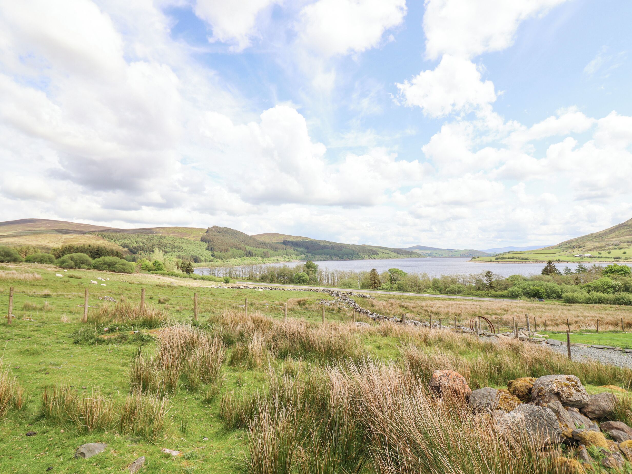 A scenic landscape with rolling hills, a lake, and a stone wall.