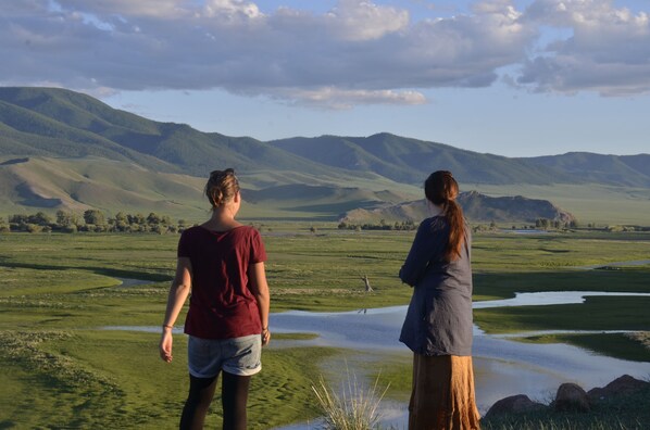 Two people standing on a grassy hill overlooking a valley with rolling hills in the background. - ViaVia Harganat Lodge (Burentogtoh)