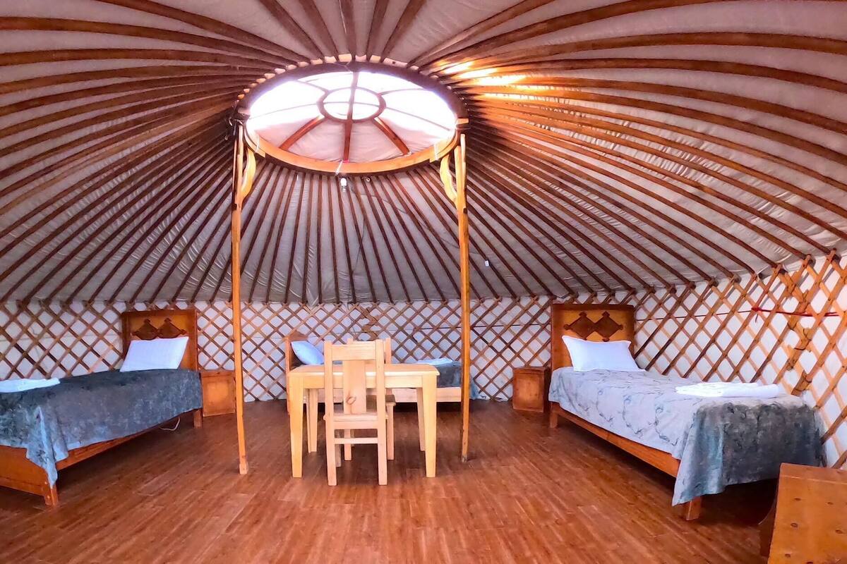 Una yurtas con dos camas, una mesa central y un dosel.