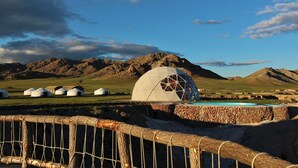 Des yourtes et une structure en forme de dôme géodésique dans un paysage montagneux.