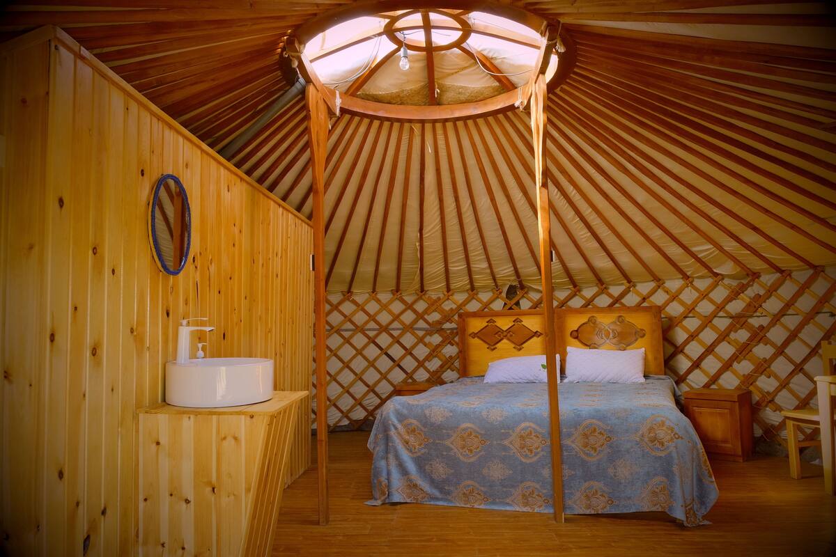 Una yurtas con cama, lavabo y techo de madera.