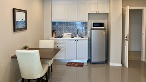 Eine moderne Küche mit weißen Schränken, einem Edelstahlkühlschrank und einer Mikrowelle. Es ist ein Esstisch mit Stühlen und ein kleiner Teppich auf dem Boden.