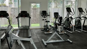 Ein Fitnessstudio mit verschiedenen Trainingsgeräten, großen Fenstern und Blick auf einen Garten.