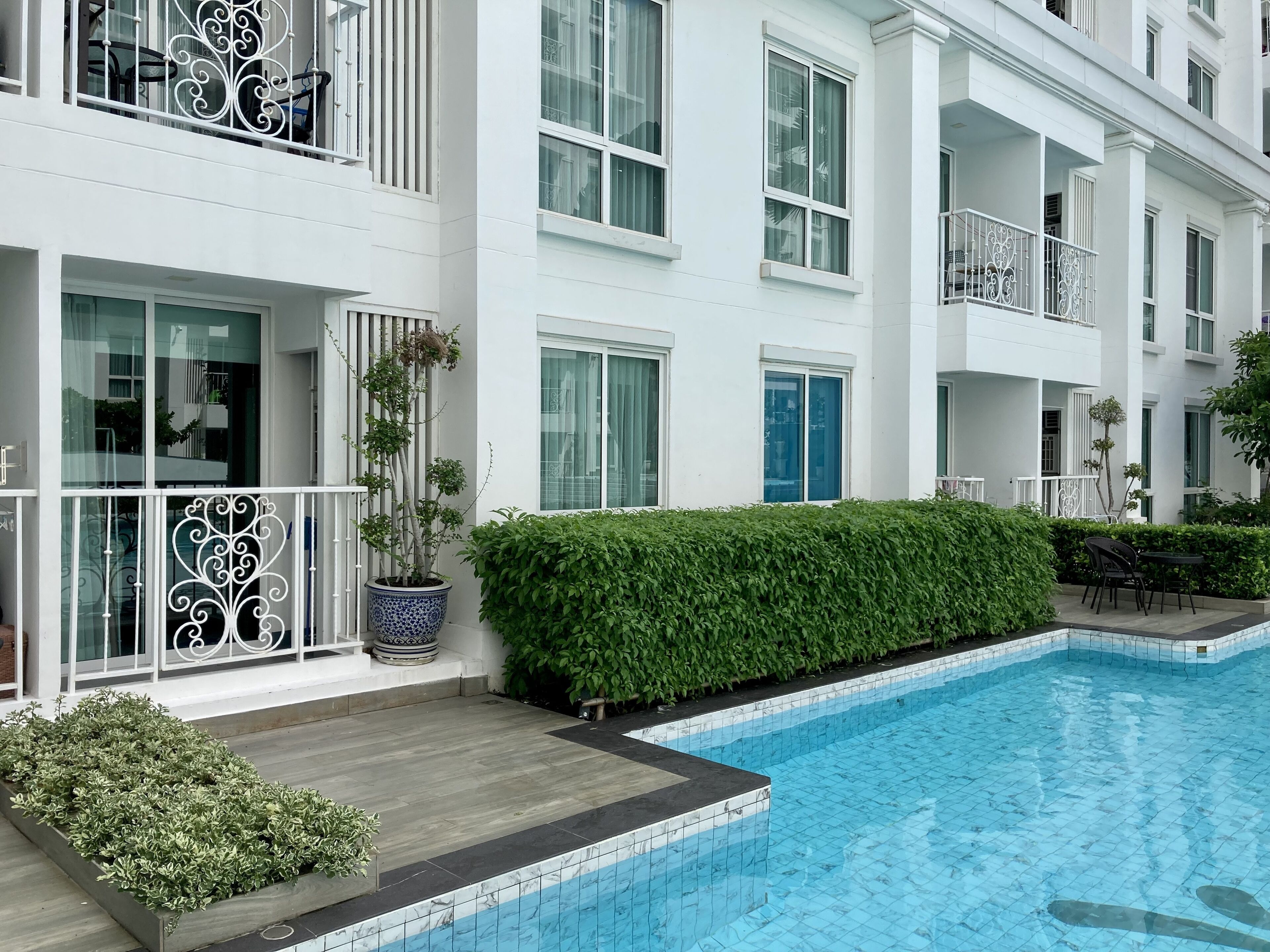 Um hotel moderno com piscina, varandas com guarda-corpos brancos e um jardim bem cuidado.