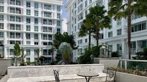Ein modernes Hotel mit Terrasse, das zwei Tische und Stühle, Palmen und ein weißes Gebäude mit Balkonen zeigt.