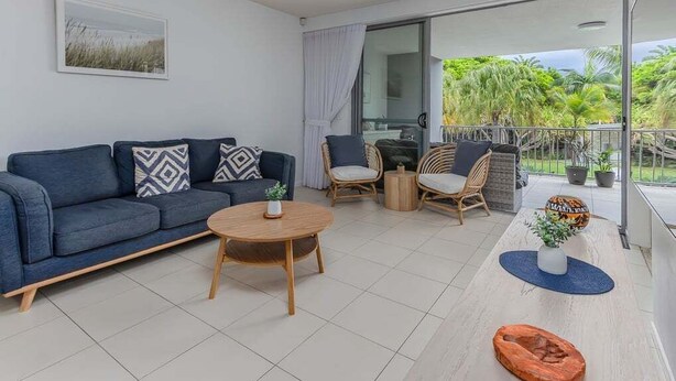 A modern living room with a sofa, chairs, a coffee table, and a balcony with plants. - 3 Bedroom Poolside Drift North Apartment (Tweed)