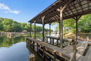 A wooden dock extending into a calm lake, supported by sturdy pillars and a covered pavilion.